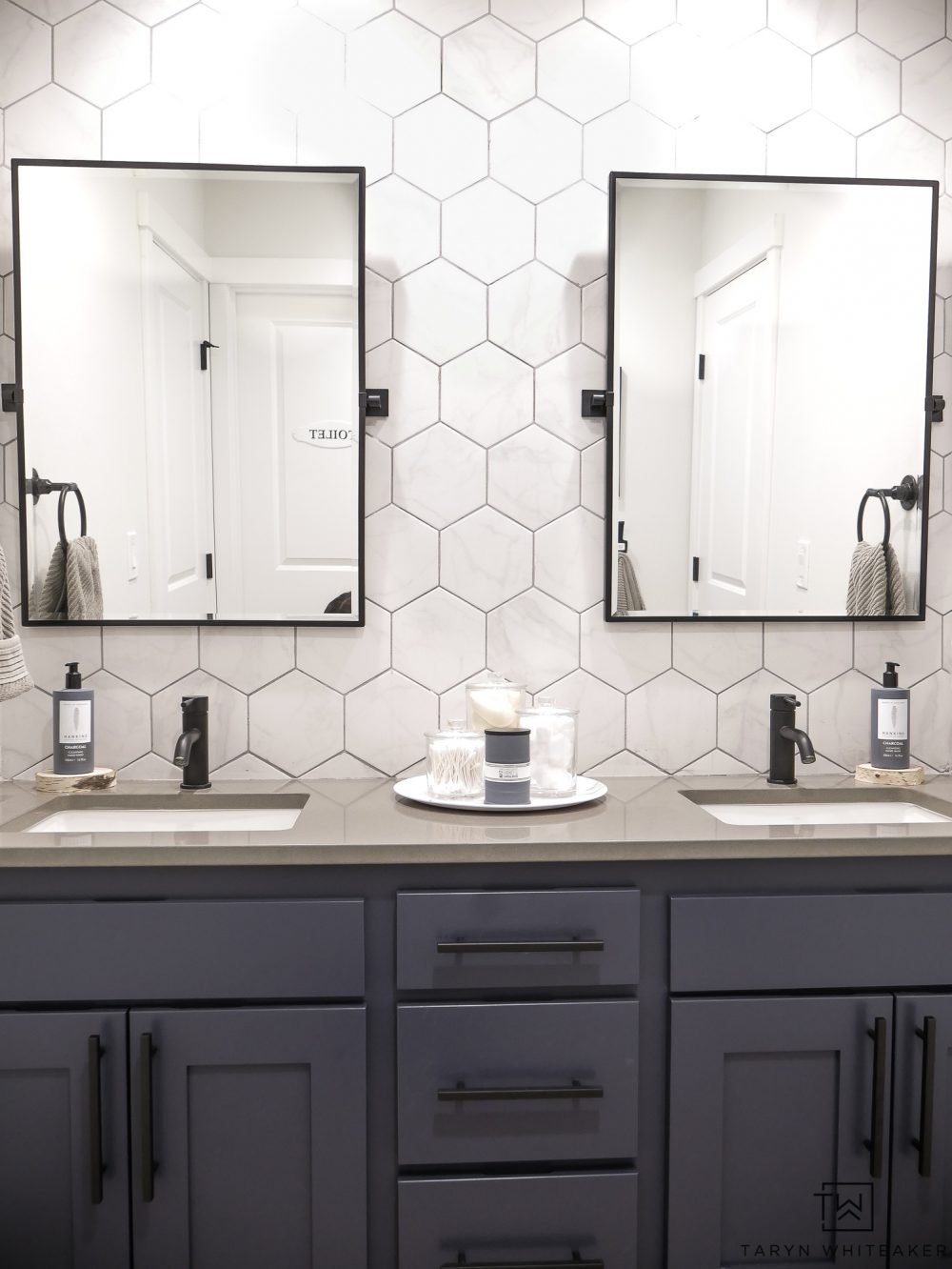 Come see what this bathroom looked like before! This double sink vanity was just a basic builder grade and now it has it's own custom modern look with marble looking hexagon tile, black pivot mirrors and charcoal blue cabinets! 