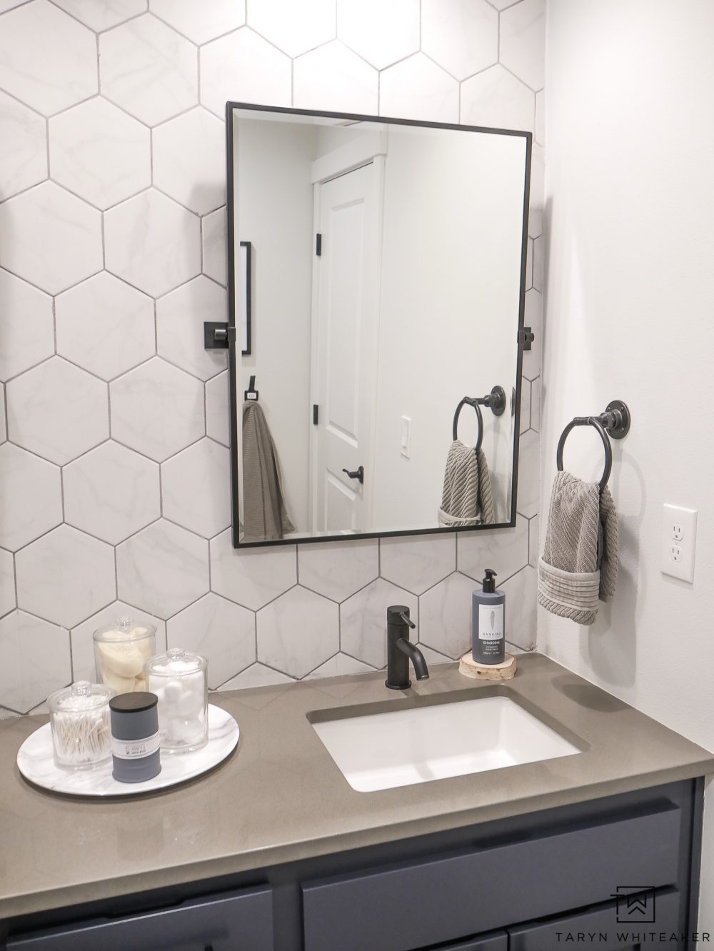 Come see what this bathroom looked like before! This double sink vanity was just a basic builder grade and now it has it's own custom modern look with marble looking hexagon tile, black pivot mirrors and charcoal blue cabinets! 