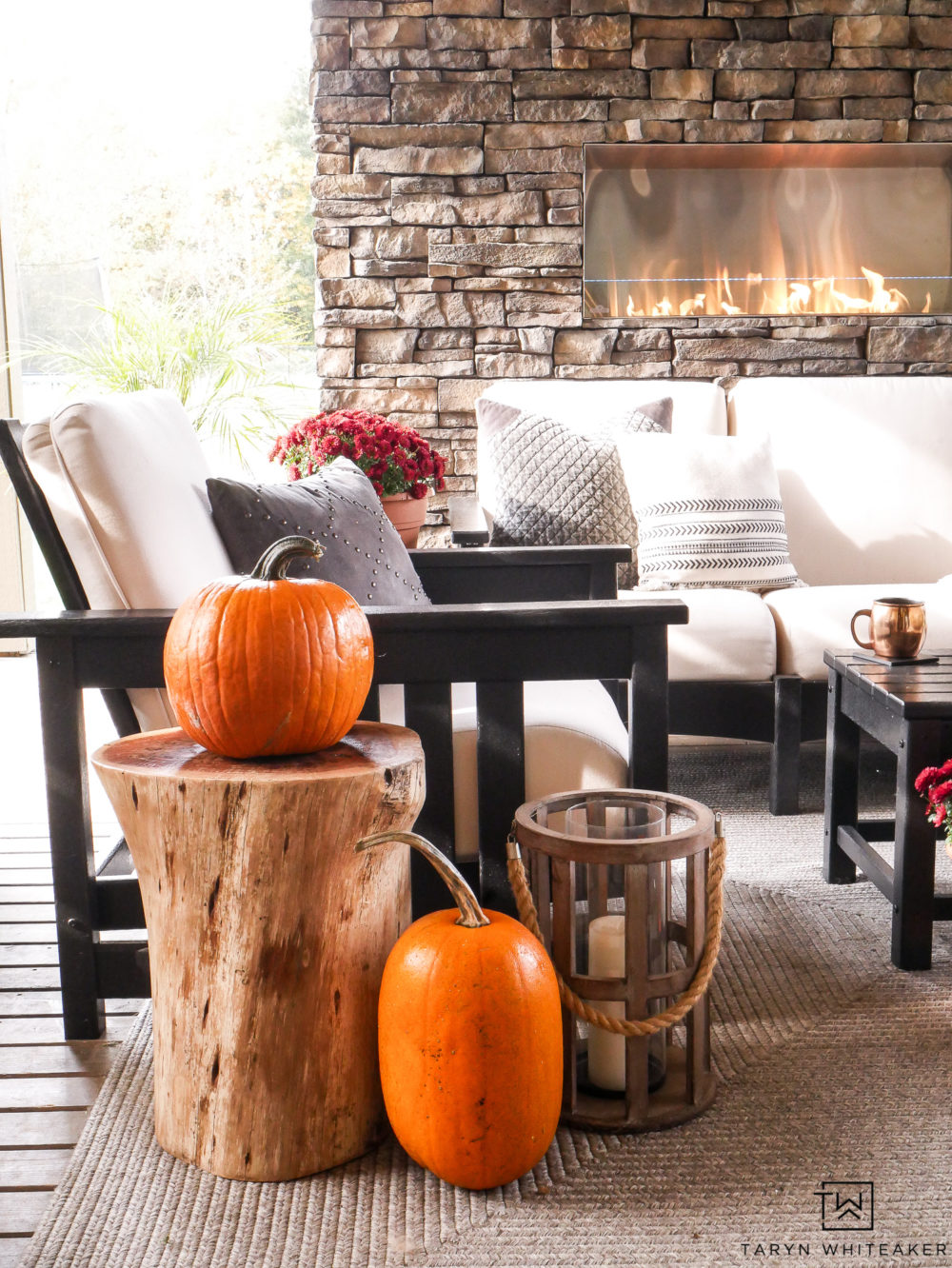 Decorating an outdoor living space for fall with pops of orange pumpkins and red mums. 