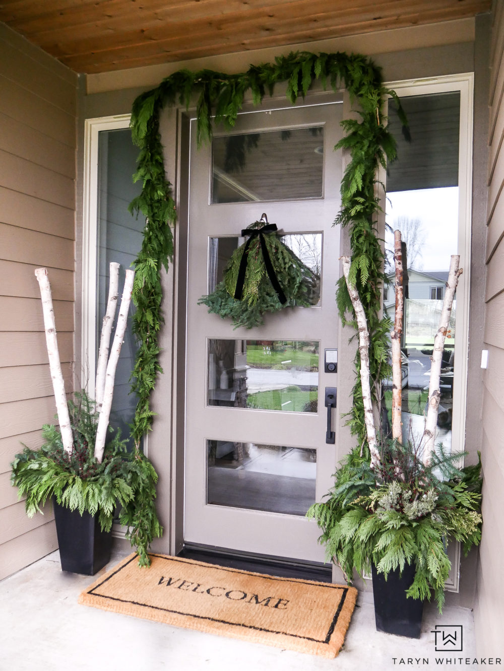 Classic Christmas Porch Decor using fresh green garland around the door and winter planters with birch logs!