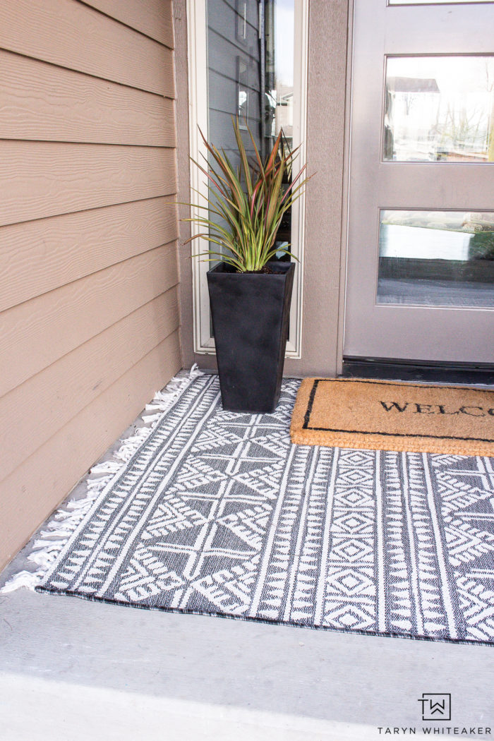 Neutral spring porch decor with layered black and white outdoor rugs and black planters. 