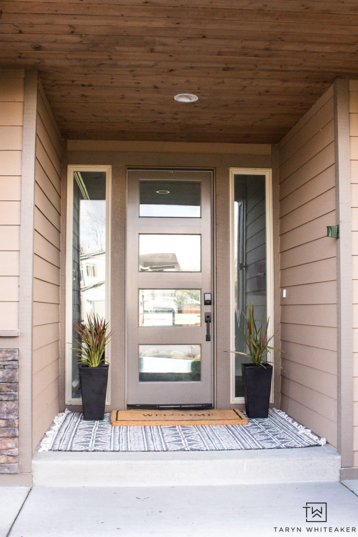 Neutral modern spring porch decor with layered black and white outdoor rugs and black planters. 