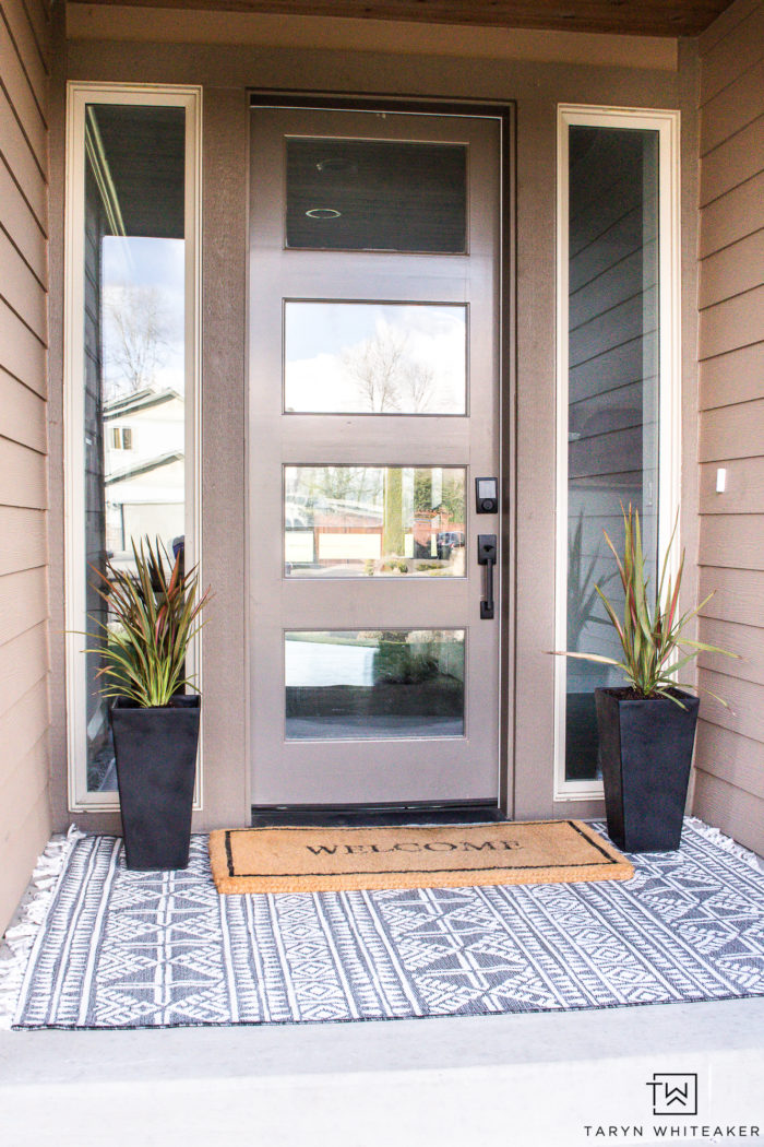 Neutral modern spring porch decor with layered black and white outdoor rugs and black planters. 