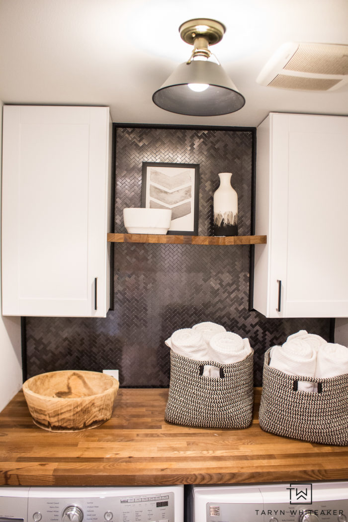 Tour this Rustic Modern Laundry Room that you can easily DIY yourself! From pre-made cabinets, butcher block countertops and peel and stick tile backsplash!