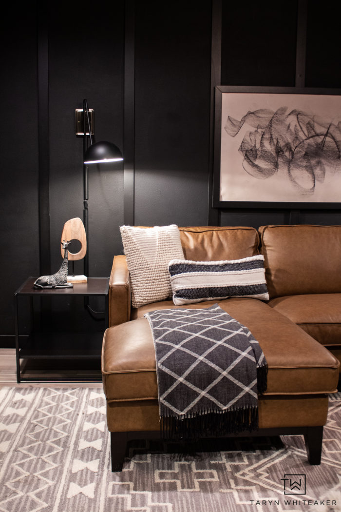 Classic mid century modern den space with dark black walls and trim and cognac leather sofa. 