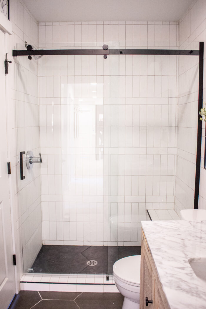 black frameless shower door with white subway tile. 