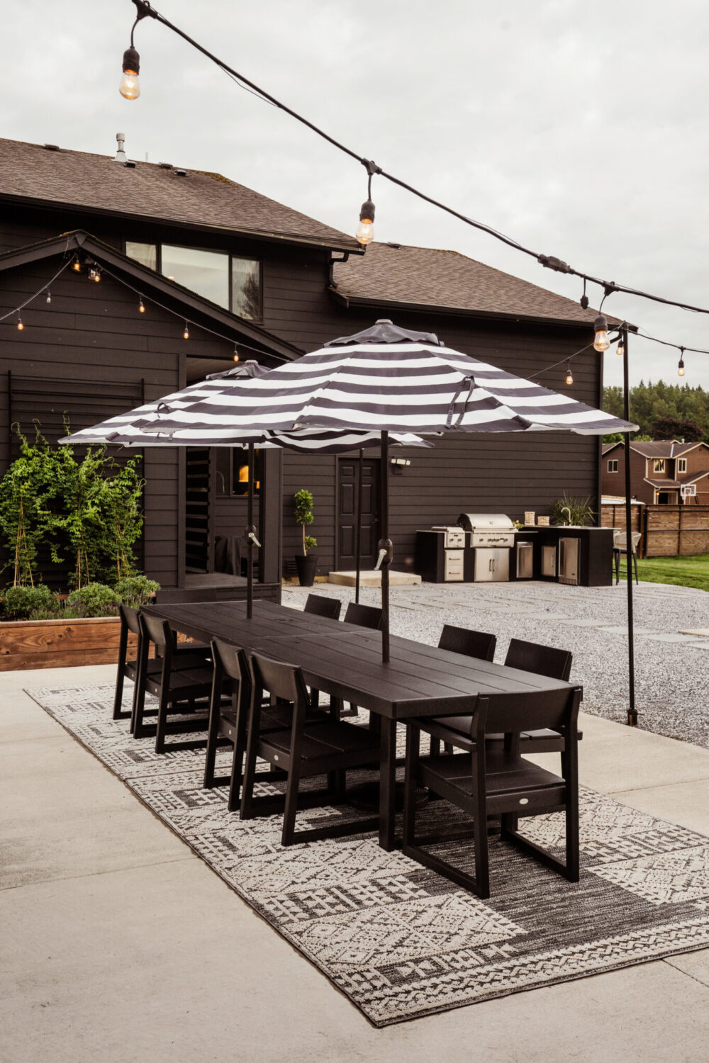 Black and white backyard design with large dining table and striped outdoor umbrellas 