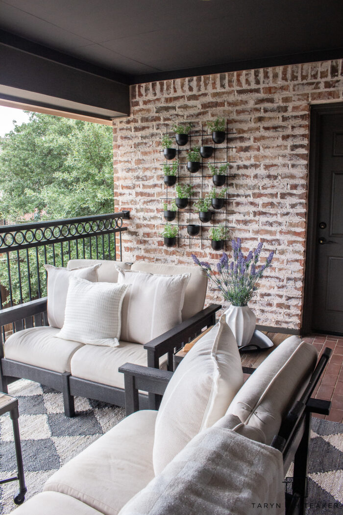 Modernize your brick patio with hanging planters, dark moody ceiling, dark trim and black metal accents. Softening the look with neutral patio furniture. 