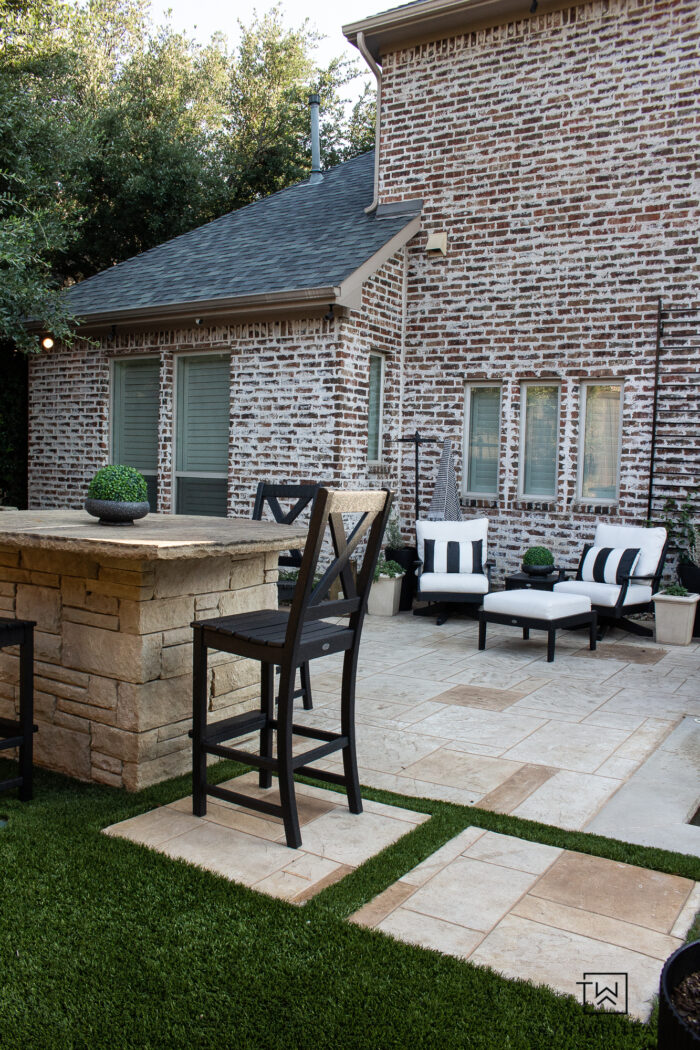 Tour this Modern English Country Backyard featuring classic black and white outdoor furniture and decor with greenery and brick exterior. 