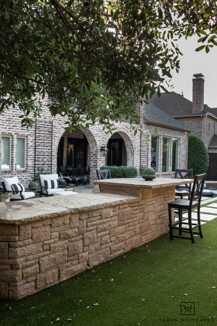Tour this Modern English Country Backyard featuring classic black and white outdoor furniture and decor with greenery and brick exterior. 