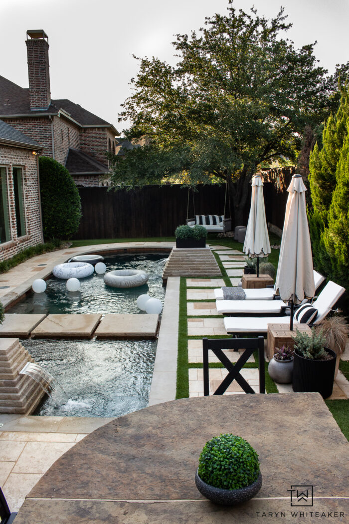 Tour this Modern English Country Backyard featuring classic black and white outdoor furniture and decor with greenery and brick exterior and oval shaped pool. 