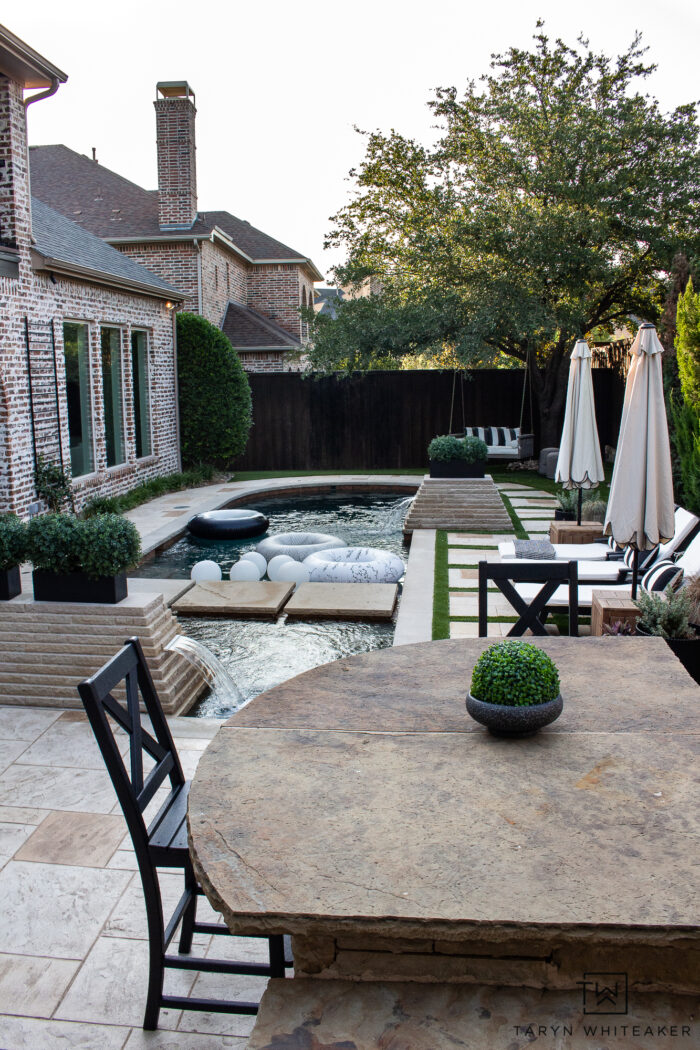 Tour this Modern English Country Backyard featuring classic black and white outdoor furniture and decor with greenery and brick exterior. 