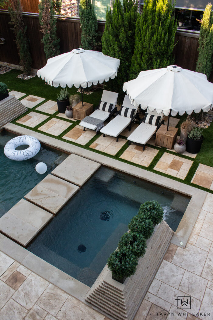 Tour this Modern English Country Backyard featuring classic black and white outdoor furniture and decor with greenery and brick exterior, oval shaped pool with pavers and turf. 