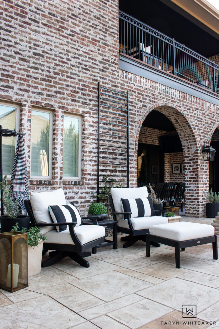 Tour this Modern English Country Backyard featuring classic black and white outdoor furniture and decor with greenery and brick exterior. 