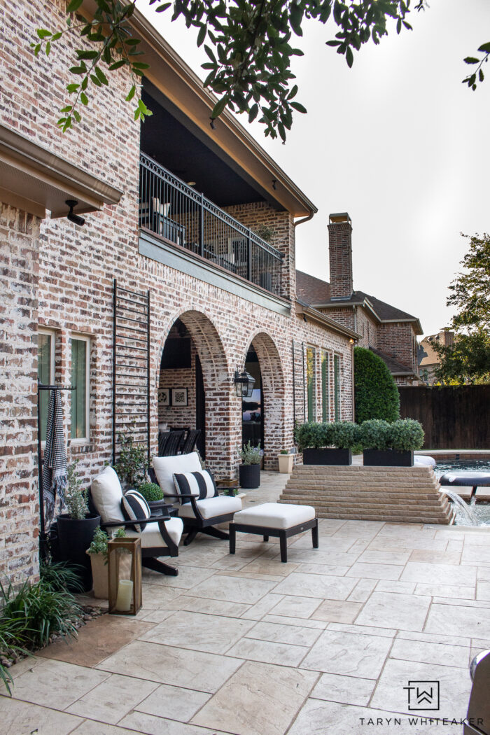 Tour this Modern English Country Backyard featuring classic black and white outdoor furniture and decor with greenery and brick exterior. 