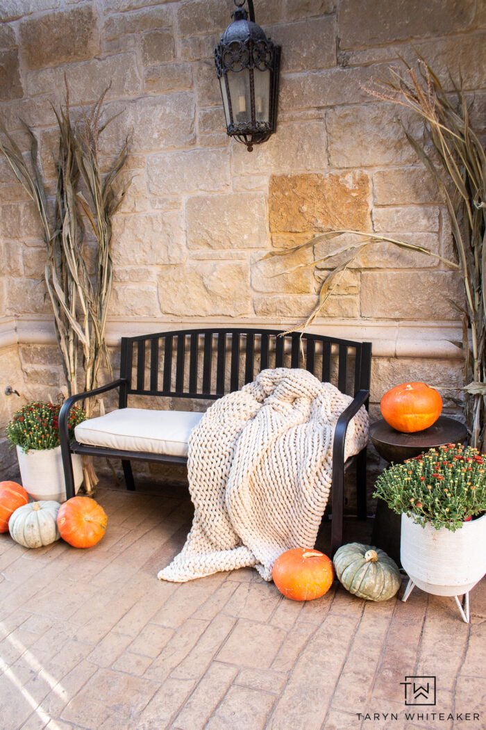 Cozy fall bench display with cozy blanket, corn stalks, heirloom pumpkins and mums. The perfect simple fall entry display. 