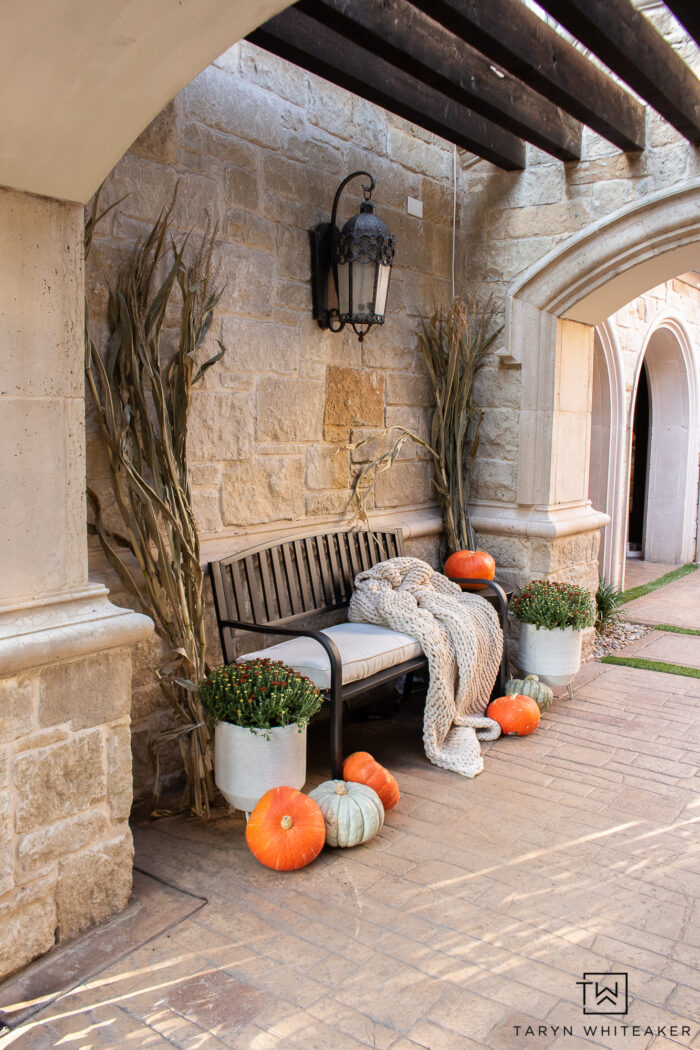 Cozy fall bench display with cozy blanket, corn stalks, heirloom pumpkins and mums. The perfect simple fall entry display. 