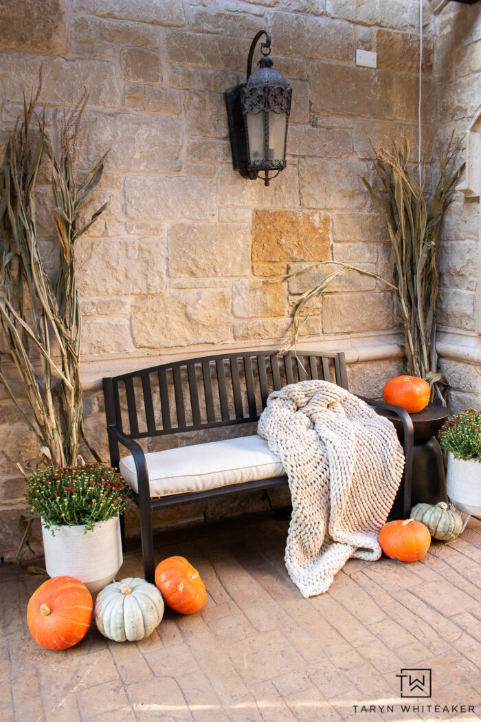 Cozy fall bench display with cozy blanket, corn stalks, heirloom pumpkins and mums. The perfect simple fall entry display. 