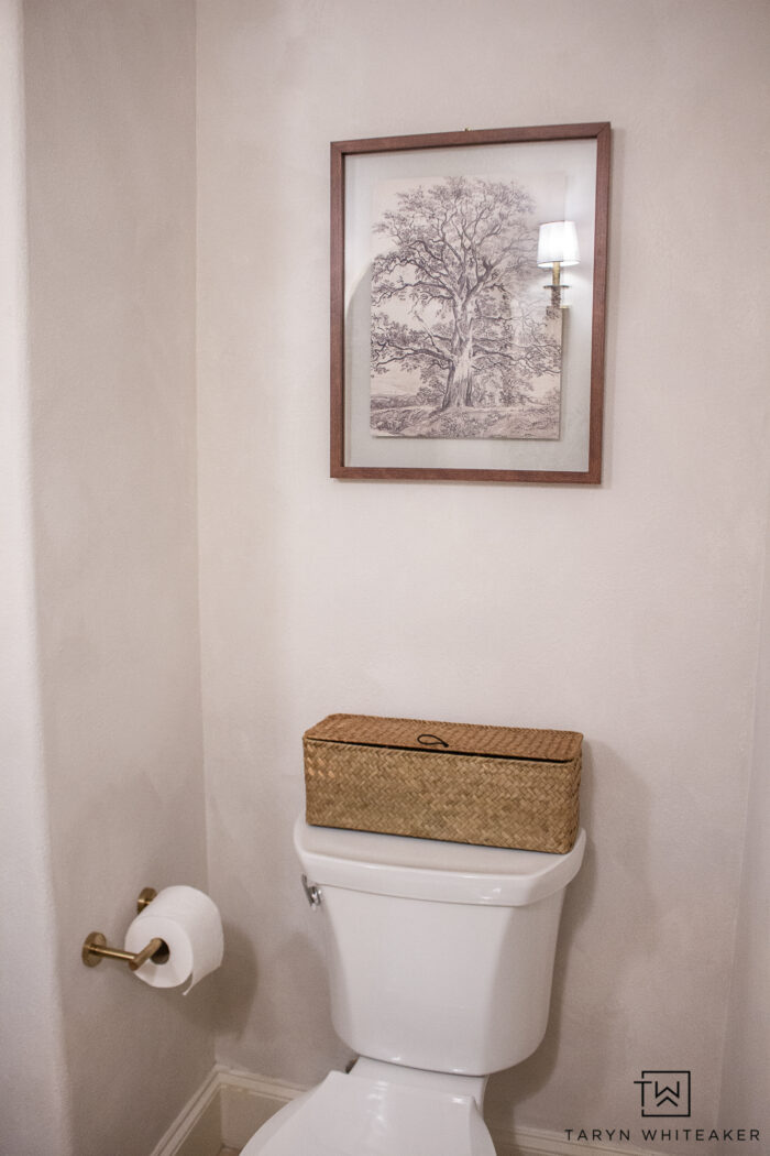 Decorating around a toilet with artwork and basket for toilet paper